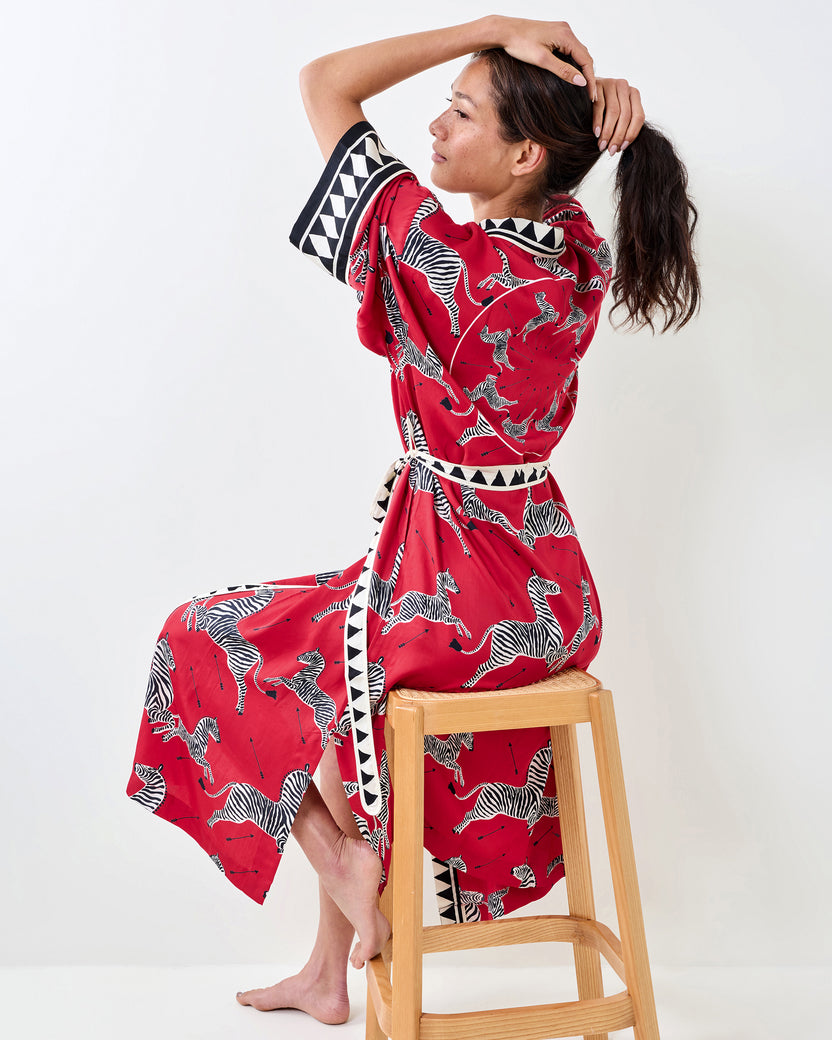 Side and back view of a person wearing a red zebra-print robe with a tied waist belt while seated on a stool.
