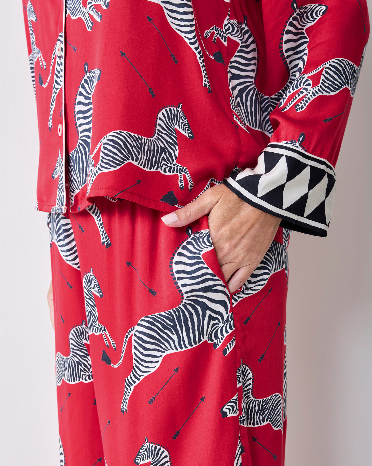 Close-up of a hand in the pocket of red zebra-print pajama pants beside the geometric-trim shirt cuff.