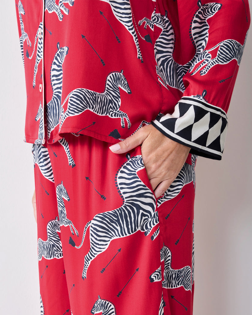 Close-up of a hand in the pocket of red zebra-print pajama pants beside the geometric-trim shirt cuff.