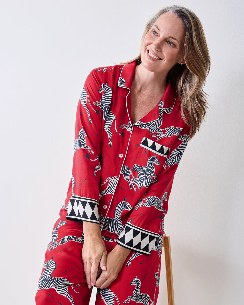Three-quarter view of a person wearing the red zebra-print pajama set while seated on a stool.