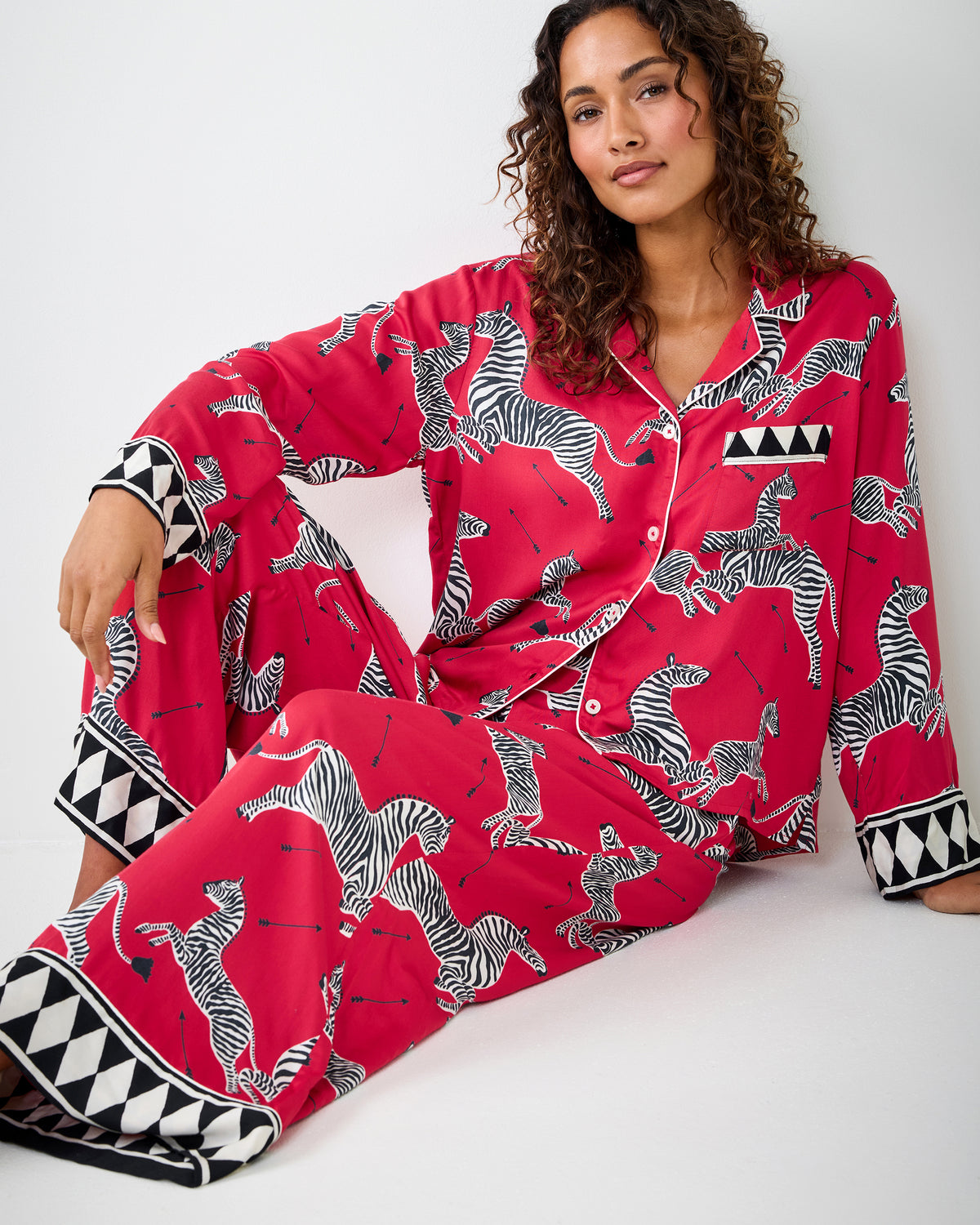 Person seated on the floor wearing the red zebra-print pajama set with geometric-trim cuffs and hems.