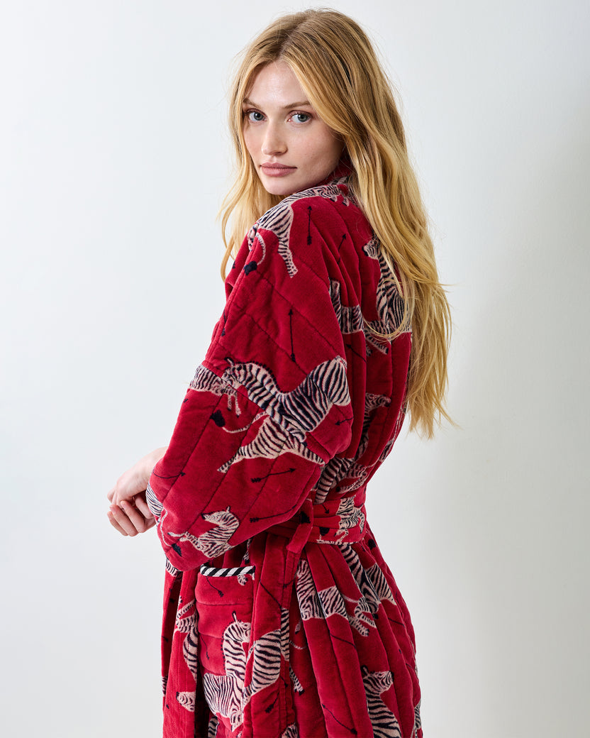 Side and back view of a person wearing a red zebra-print quilted robe with a tied belt.