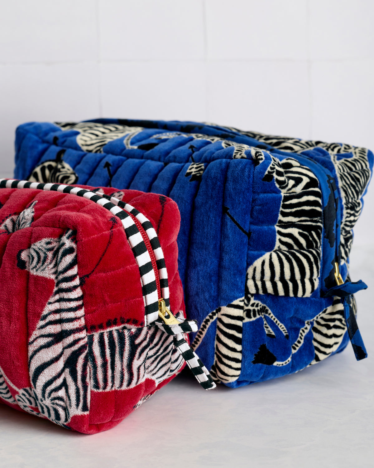 Close-up side view of red and blue quilted zebra-print pouches with striped ties and gold hardware.