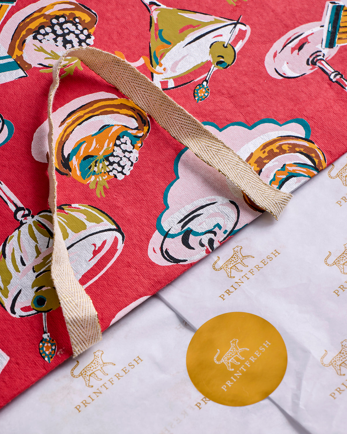 Close-up of a red printed gift bag with a sparkly handle, beside Printfresh tissue paper and a round sticker.