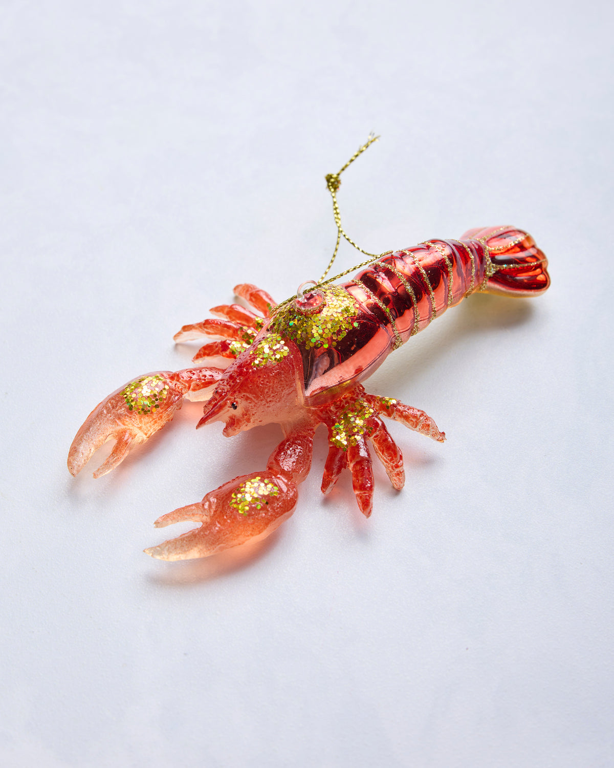 Angled view of a red glass lobster ornament with glittered details and a hanging loop.