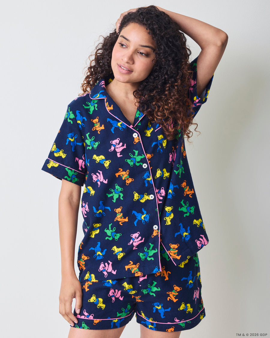 Three-quarter view of a person wearing a navy short pajama set with a multicolor dancing-bear print, button-front top, and matching shorts.
