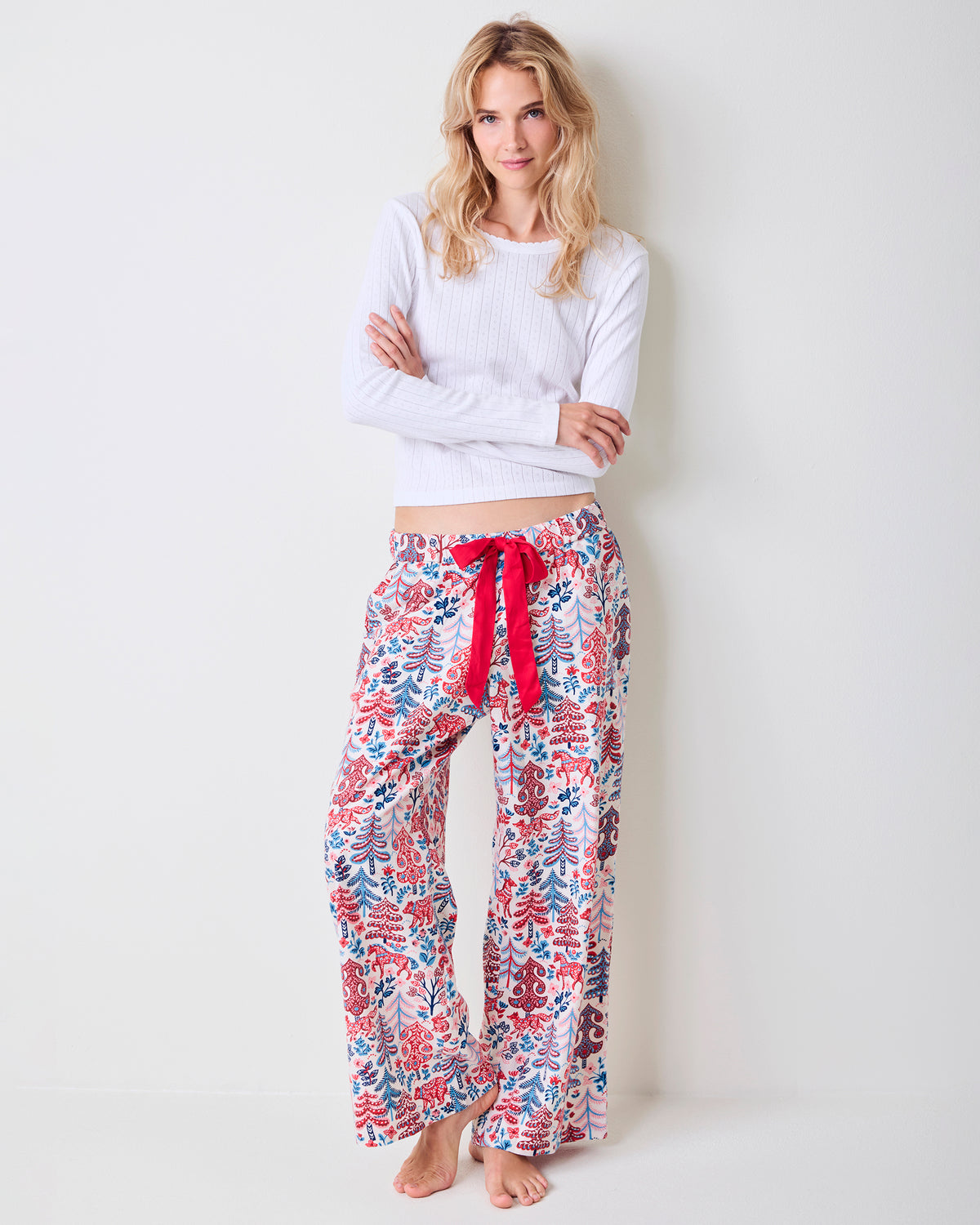 Adult model standing in cream Folklore Forest printed pajama pants with a red drawstring and a white sweater.