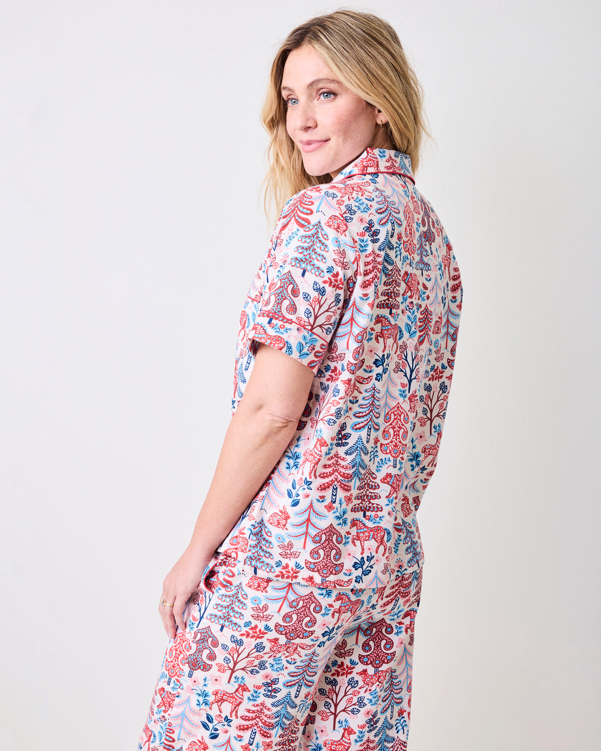 Back view of the cream short-sleeve pajama top and cropped pants with a red and blue forest-inspired print.