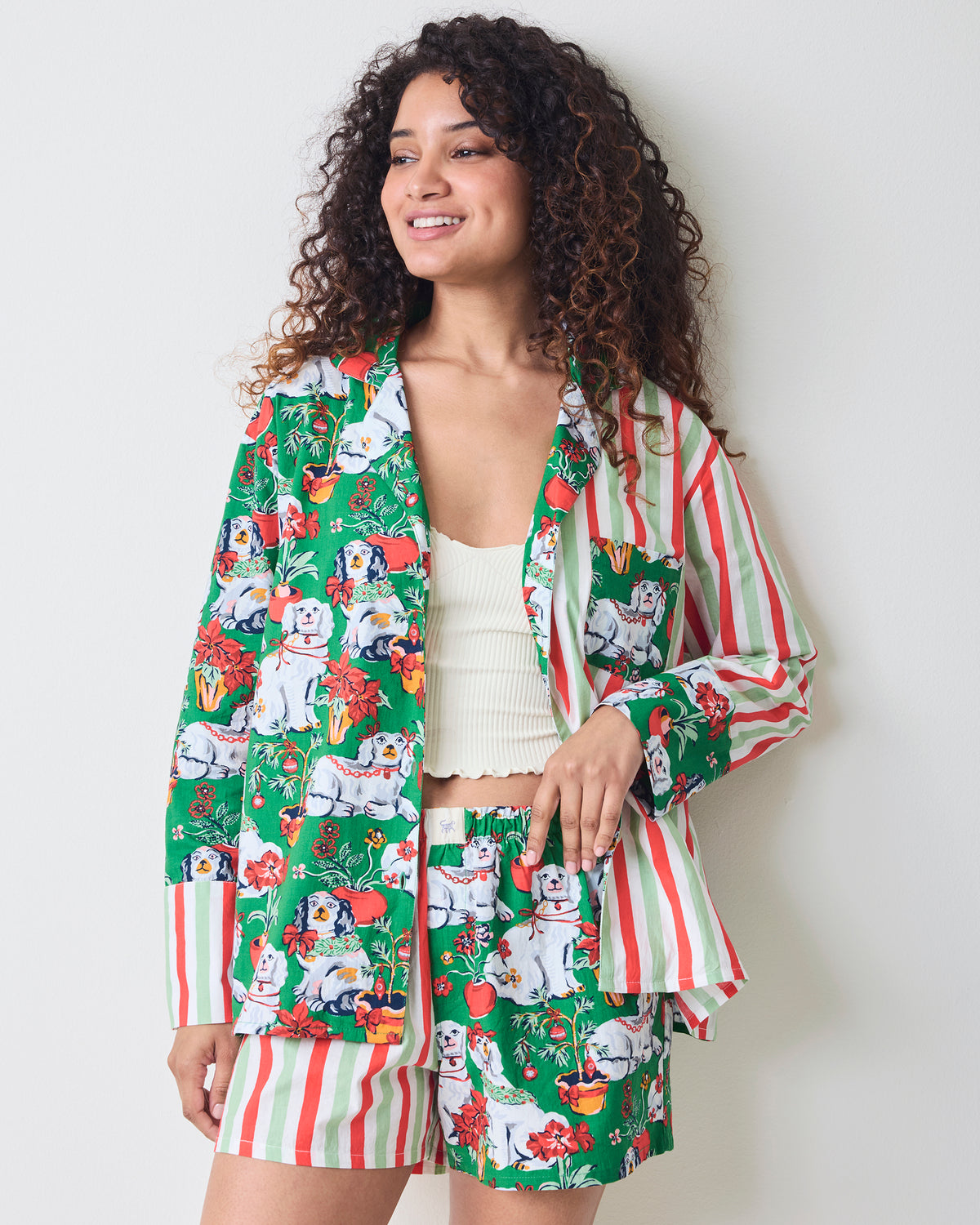 Front three-quarter view of the Good Dog Christmas Reese boxer pajama set with a green dog-and-poinsettia print and striped sleeves and shorts.
