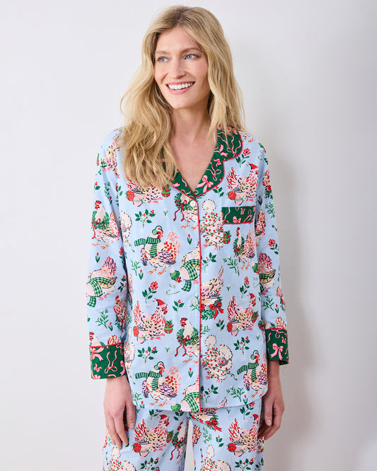 Front upper-body view of a person wearing the pale blue Holiday Hens pajama top with a button front, contrasting collar and cuffs, and chest pocket.