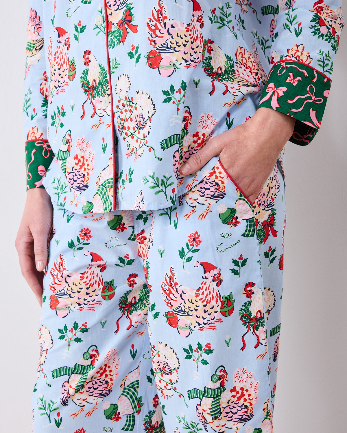 Close-up of the pale blue Holiday Hens pajama set showing the button-front top, pants, pockets, hen print, and contrasting green cuffs.