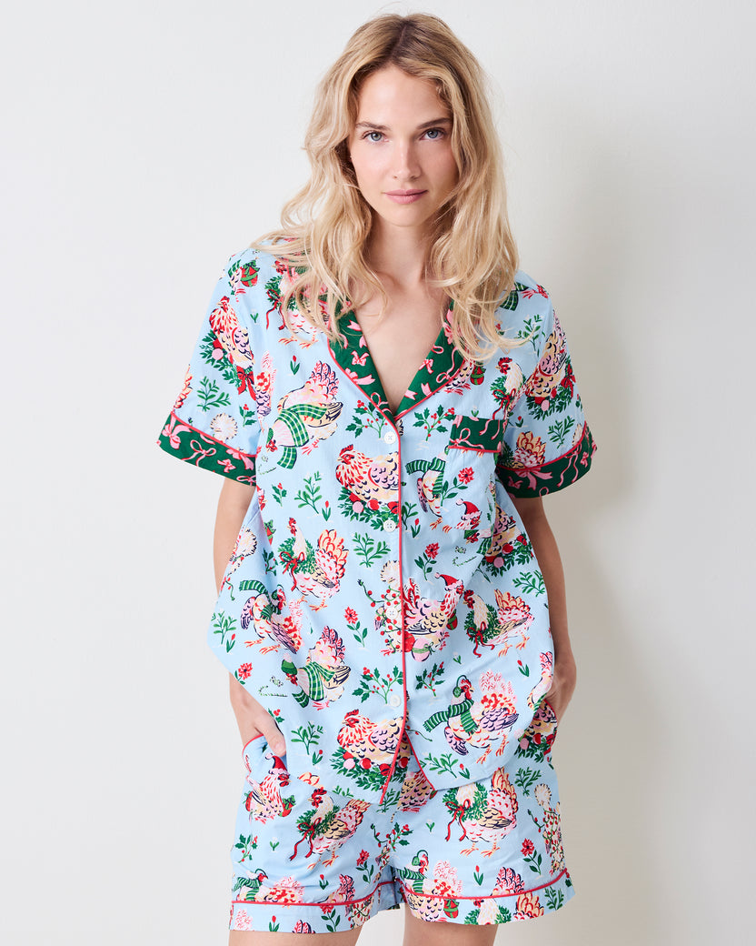 Front view of a person wearing the pale blue Holiday Hens short pajama set with a printed button-down top and shorts.