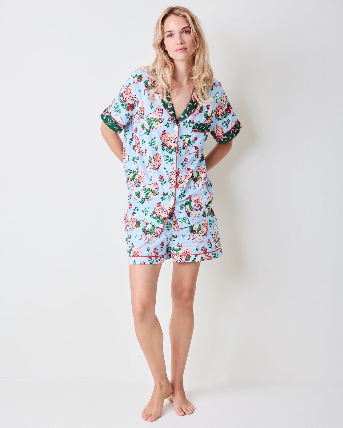 Person modeling a pale blue short pajama set with printed hens, flowers, and green trim, shown full length.