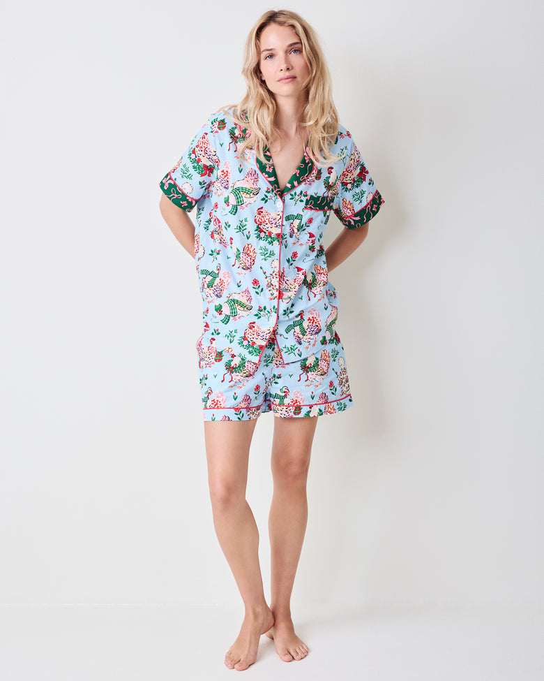 Person modeling a pale blue short pajama set with printed hens, flowers, and green trim, shown full length.