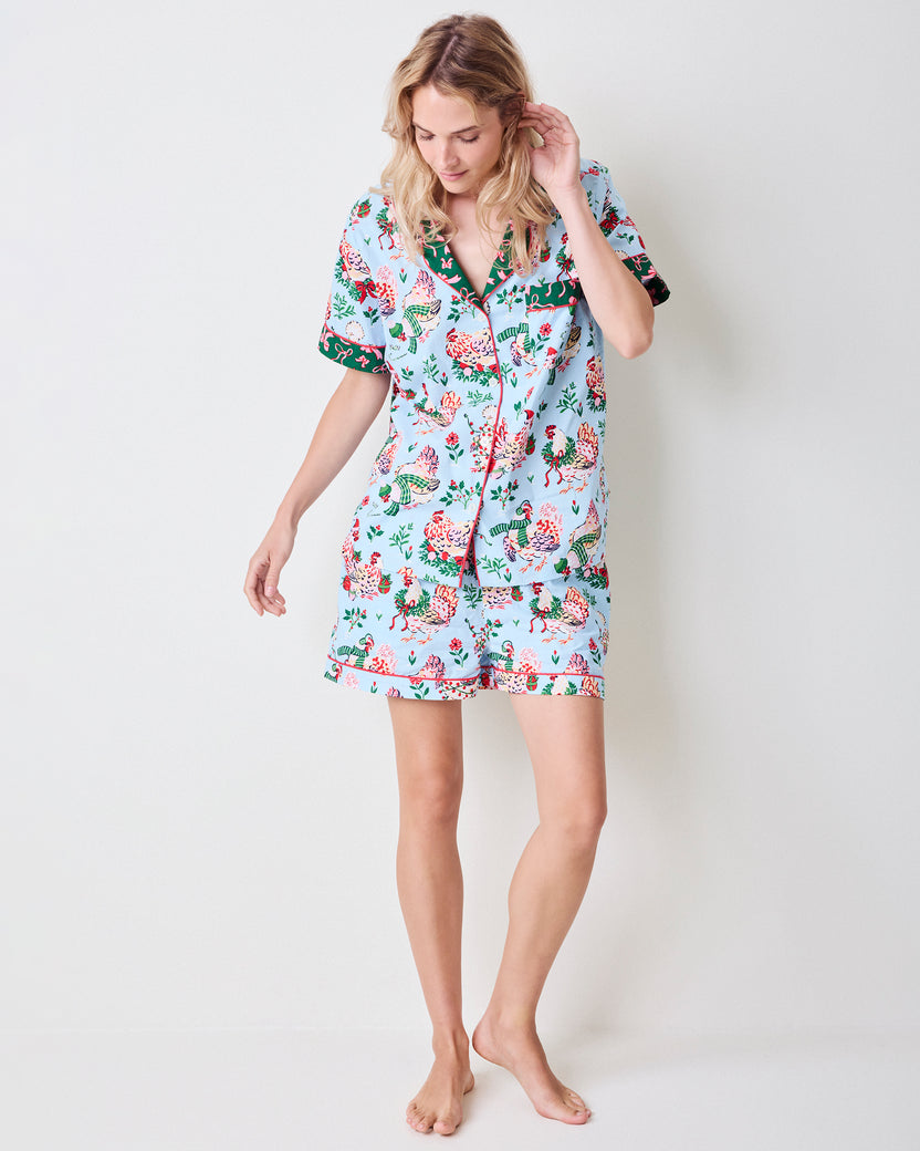 Person wearing a pale blue Holiday Hens short pajama set with a button-down top and shorts, shown from the front.