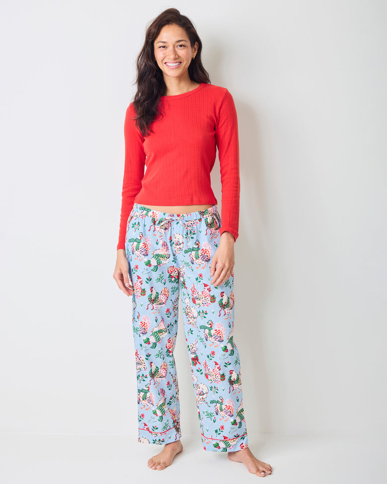 Front view of a person wearing pale blue Holiday Hens full-length pajama pants with a repeated hen and floral print.