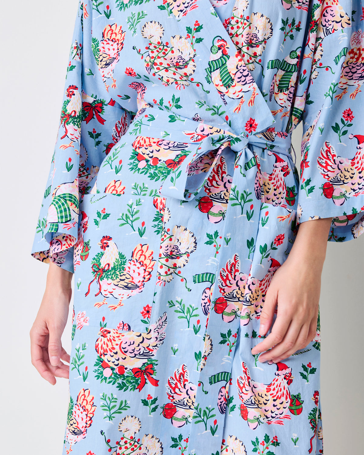 Close view of the pale blue Holiday Hens long robe showing its tie belt, side pockets, and chickens wearing winter hats and scarves.