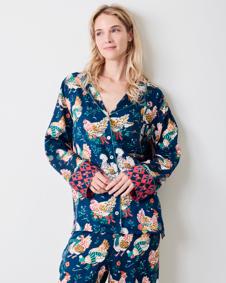 Standing model wearing a navy button-front pajama set with festive hen print and red patterned cuffs.