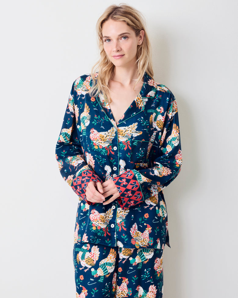 Model standing in a navy pajama set with festive hen print, white piping, and red patterned cuffs.