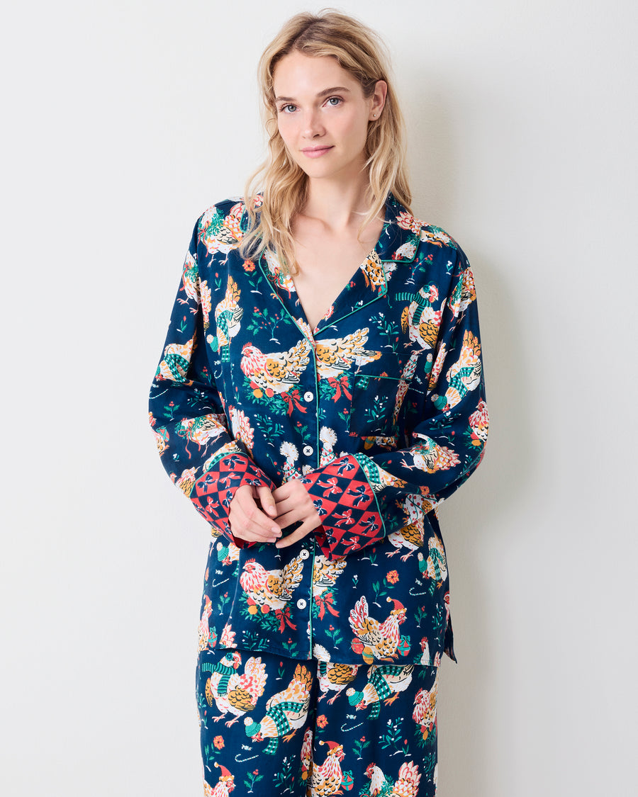 Model standing in a navy pajama set with festive hen print, white piping, and red patterned cuffs.
