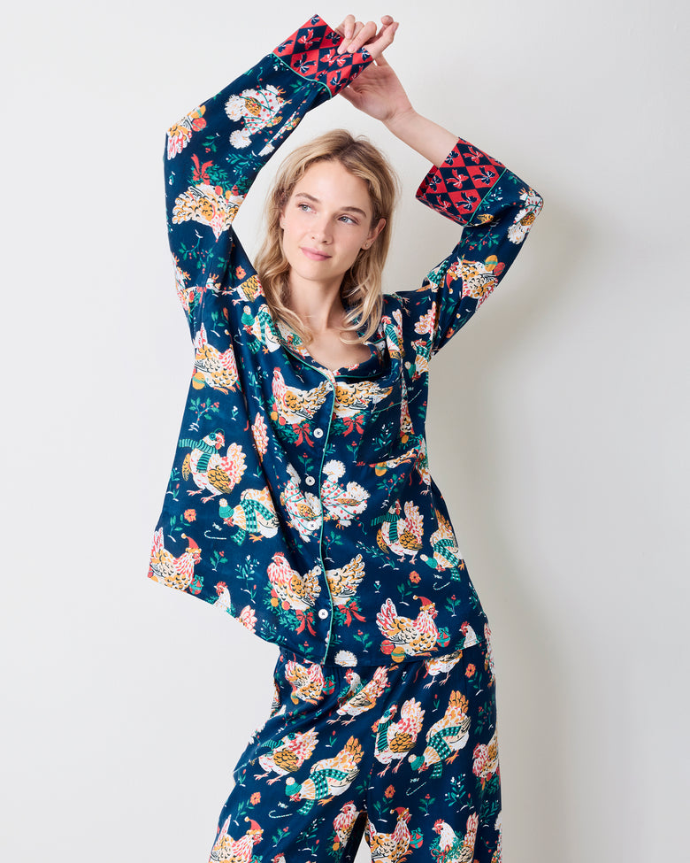 Model wearing a navy hen-print pajama set with arms raised, showing the red patterned cuffs and matching pants.
