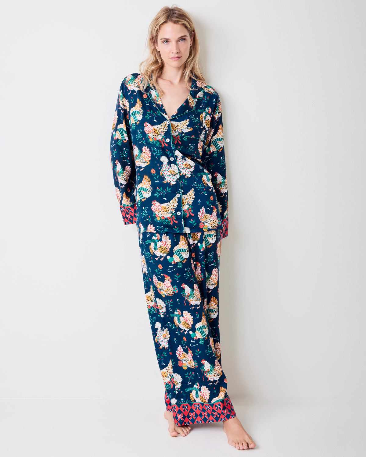 Full-length front view of a model wearing a navy pajama set with festive hen print and red patterned cuffs.
