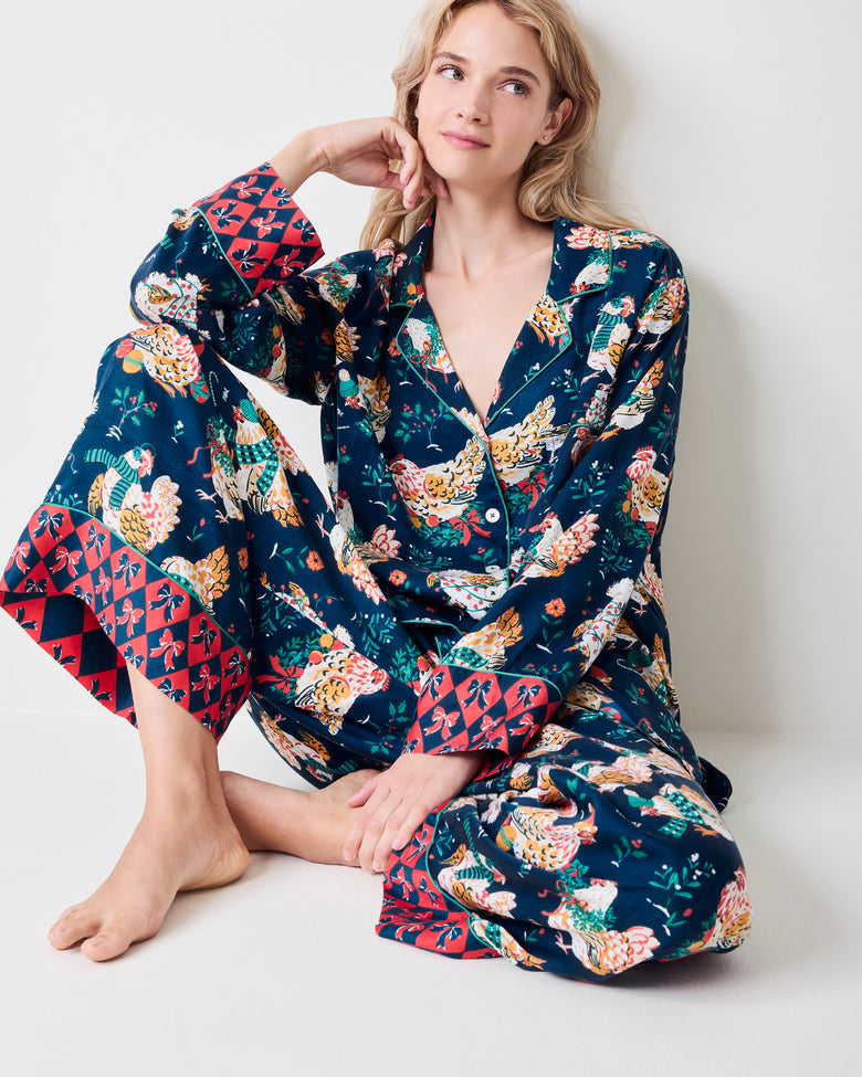 Model wearing a navy pajama set with a colorful hen print and contrasting red patterned cuffs.