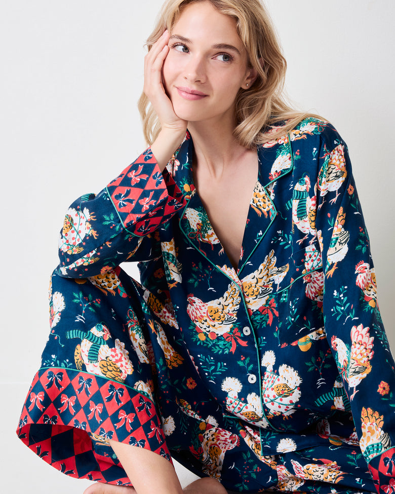 Close view of a navy pajama top with a colorful hen print, notched collar, buttons, and contrasting red patterned cuffs.