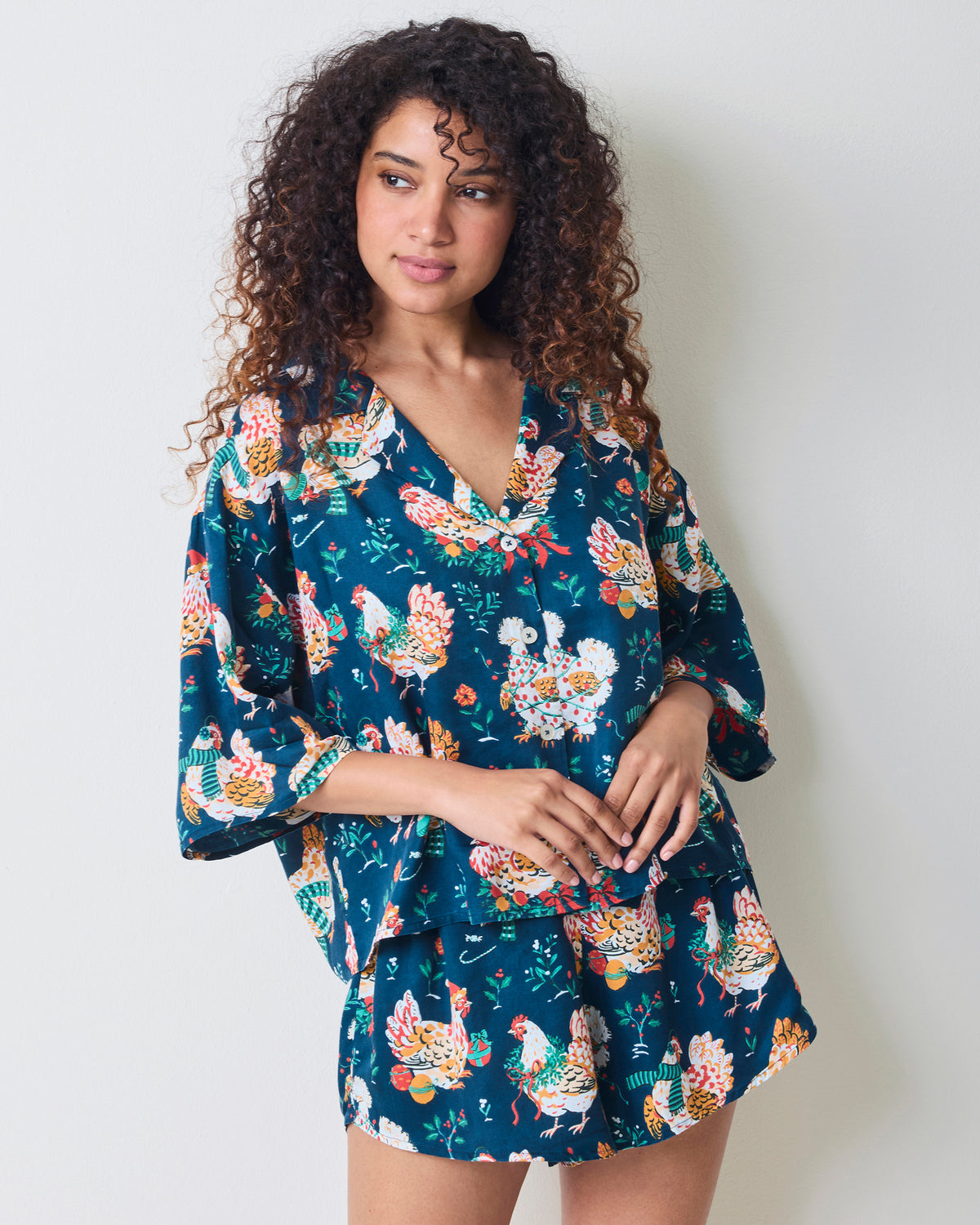 Three-quarter front view of a model wearing the Holiday Hens pajama set with a V-neck top and matching shorts.