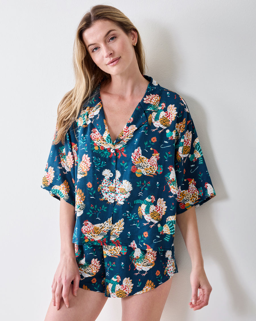Front view of a model wearing the Holiday Hens pajama set with a short-sleeved button-front top and matching shorts.