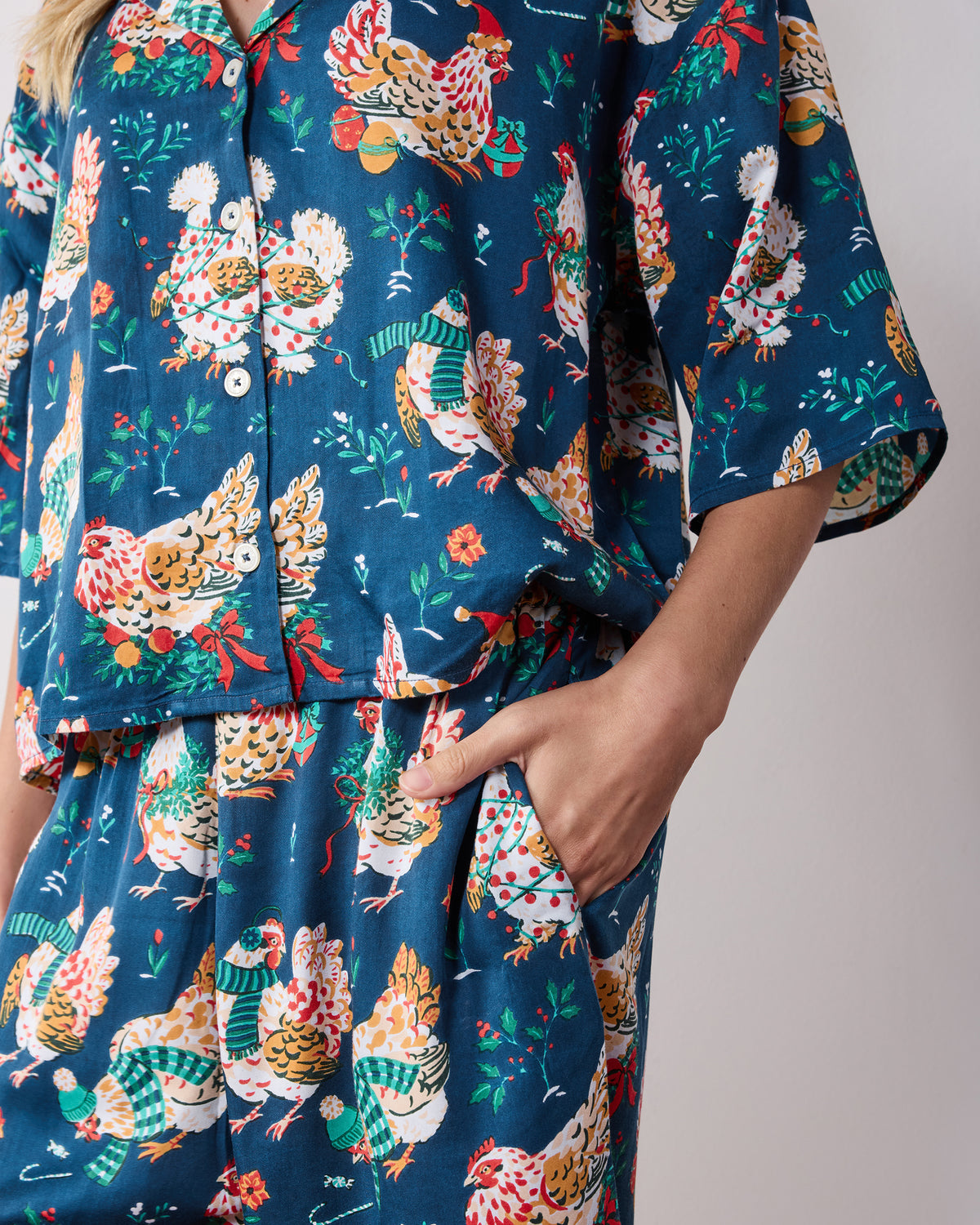 Close detail of the navy Holiday Hens pajama set showing the button-front top, wide-leg pants, side pocket, and chicken print.