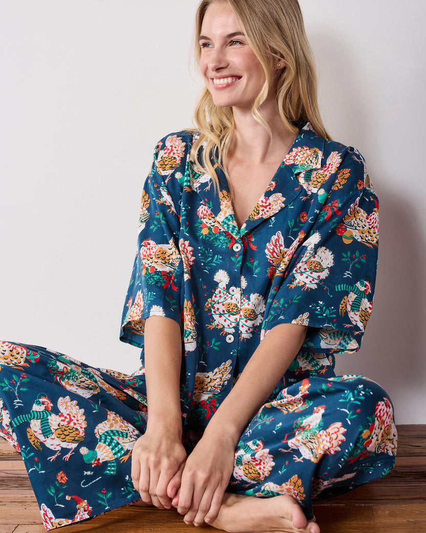 Person seated on a wooden floor wearing a navy printed button-front top with matching wide-leg pants.
