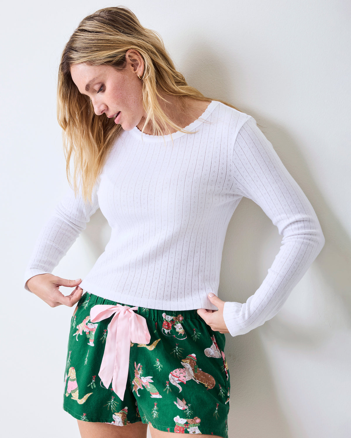 Person wearing a white long-sleeve pointelle shirt with green printed shorts, angled view.