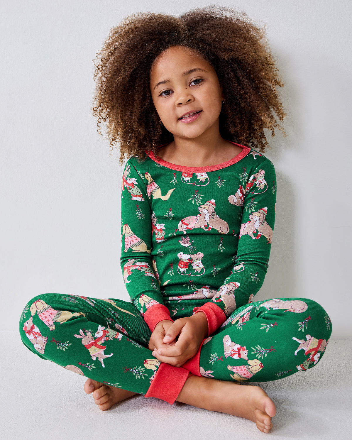 Child seated cross-legged wearing a green long-sleeve pajama top and matching pants with an illustrated holiday animal print.