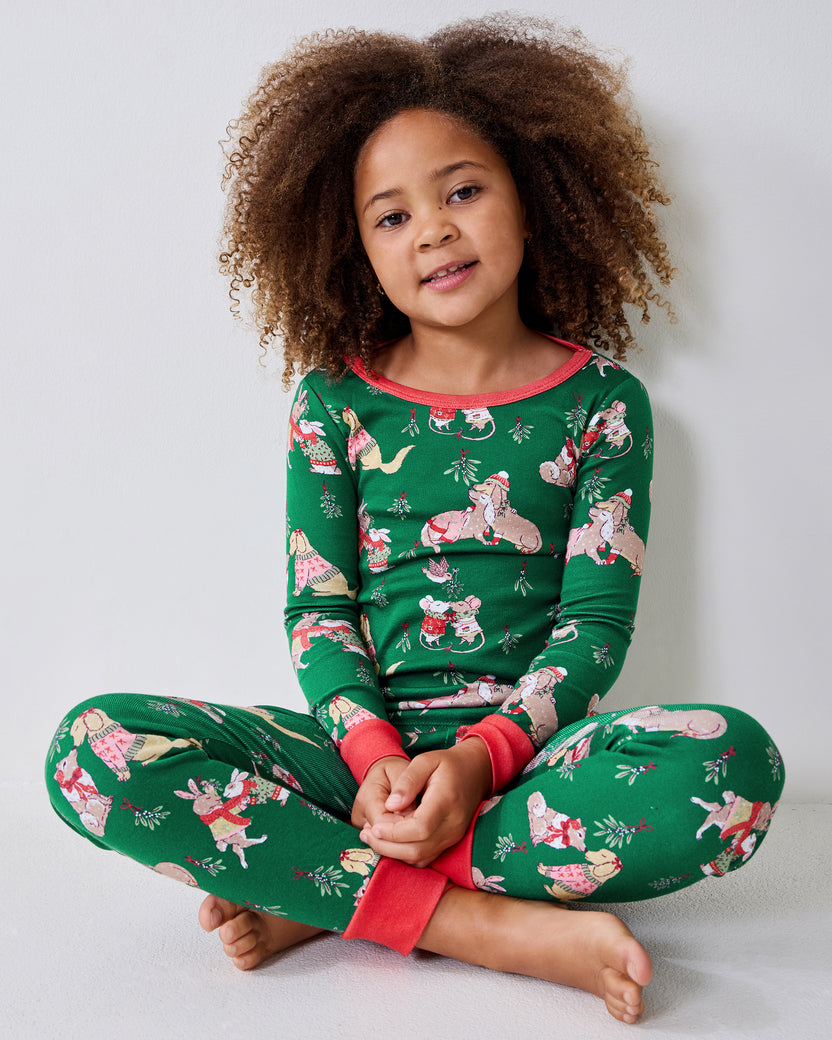 Child seated cross-legged wearing a green long-sleeve pajama top and matching pants with an illustrated holiday animal print.