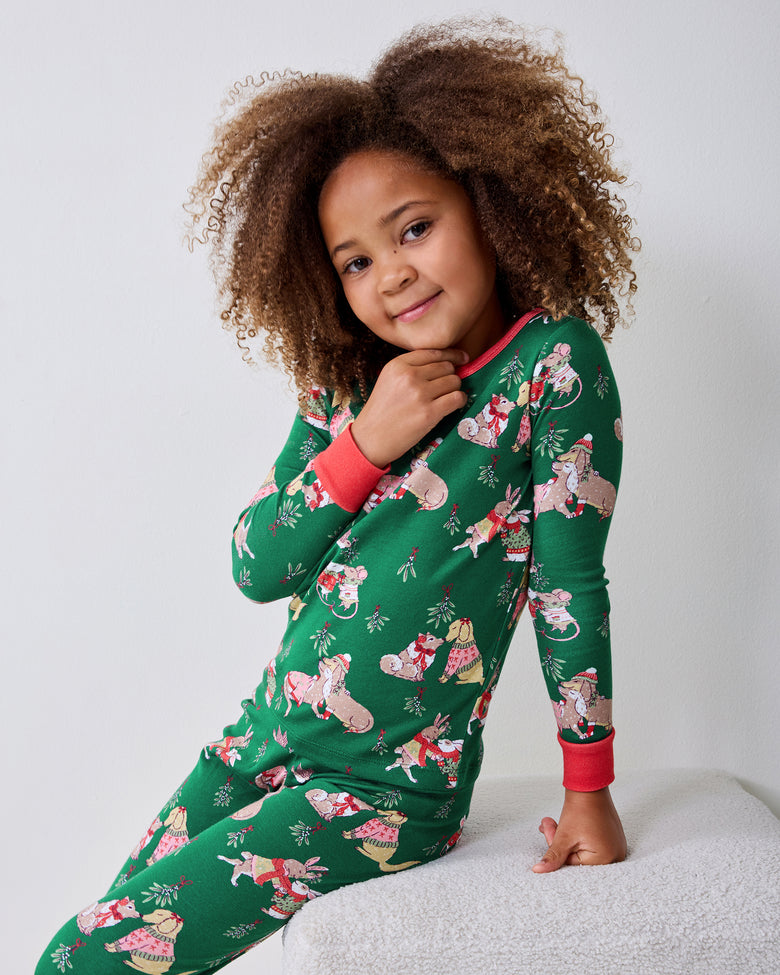 Child model seated and wearing a green long-sleeve pajama set with a repeating holiday animal print.