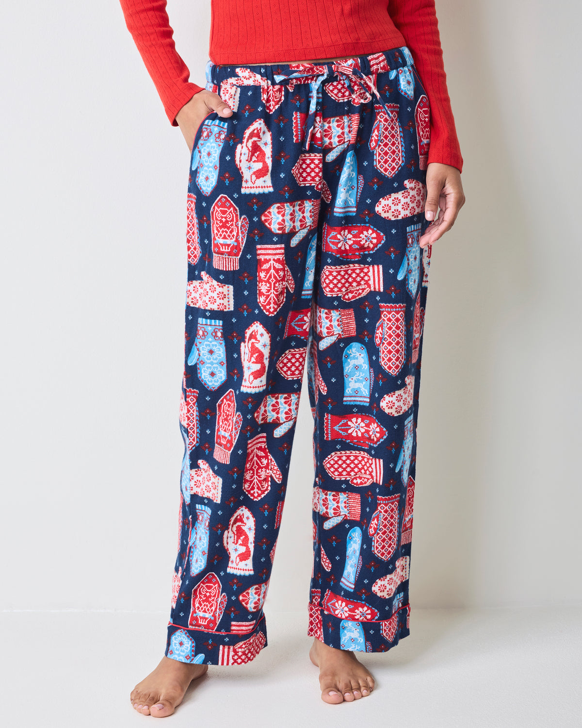 Front view of blue flannel pajama pants with a red, white, and light blue mitten print, shown on a model.