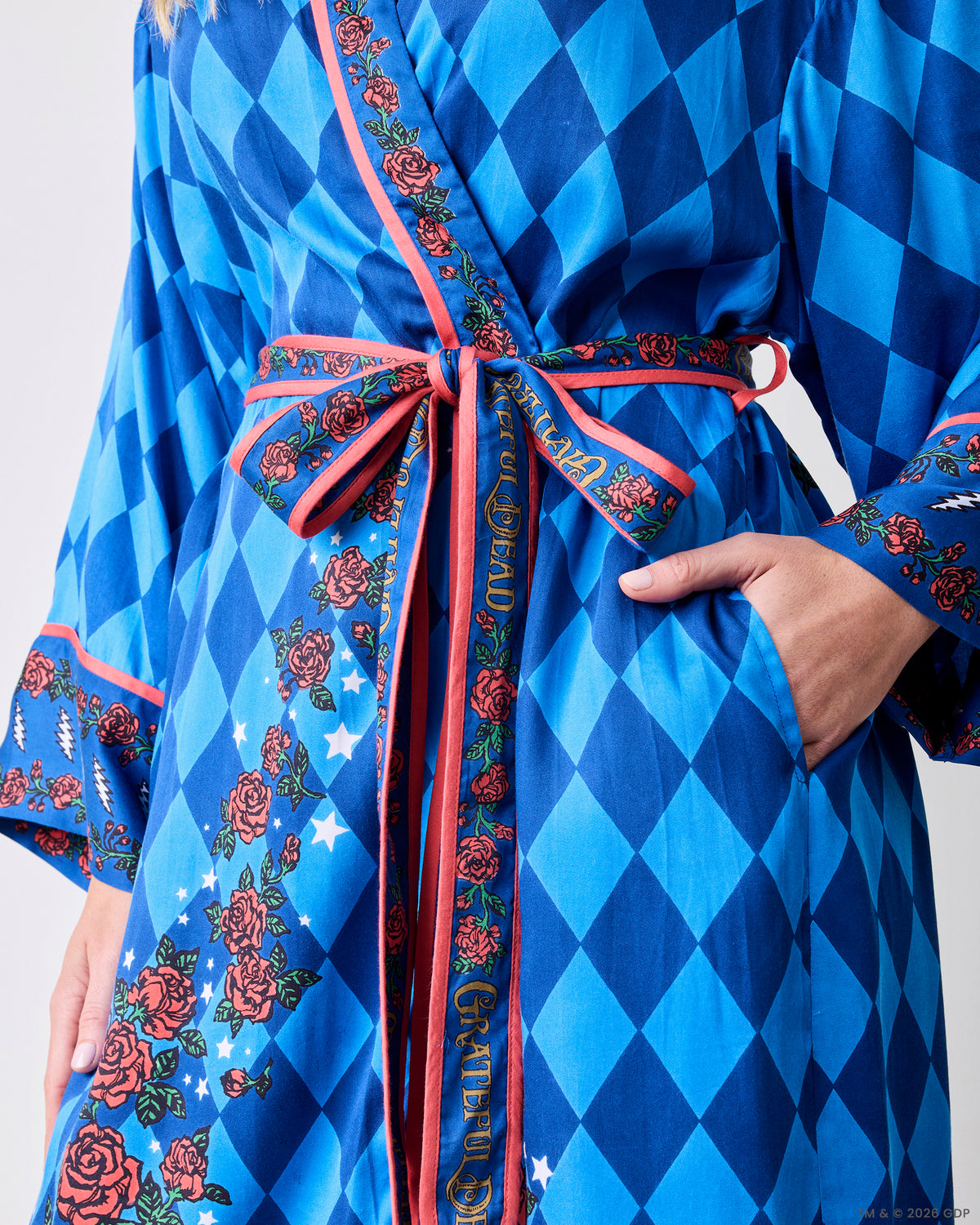 Close view of the blue patterned robe tied at the waist, showing the rose-and-star print, wide cuffs, and side pockets.