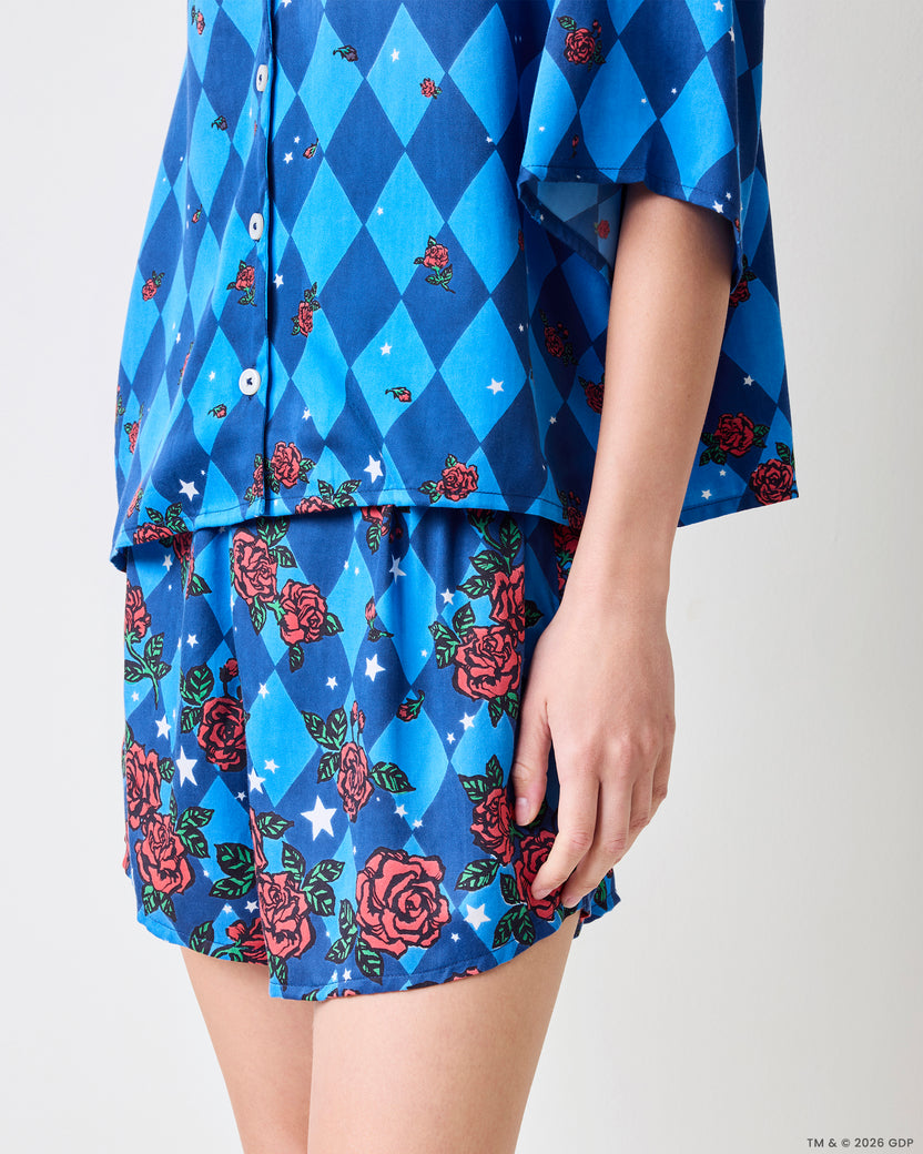 Close-up of a person wearing a blue diamond-patterned pajama top and shorts with rose and star motifs.