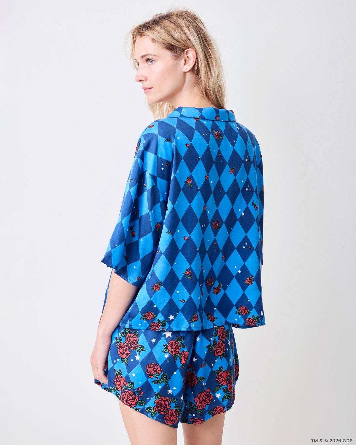 Back three-quarter view of the blue patterned Sweet Dreams Set, showing the loose button-front top and matching rose-and-star shorts.