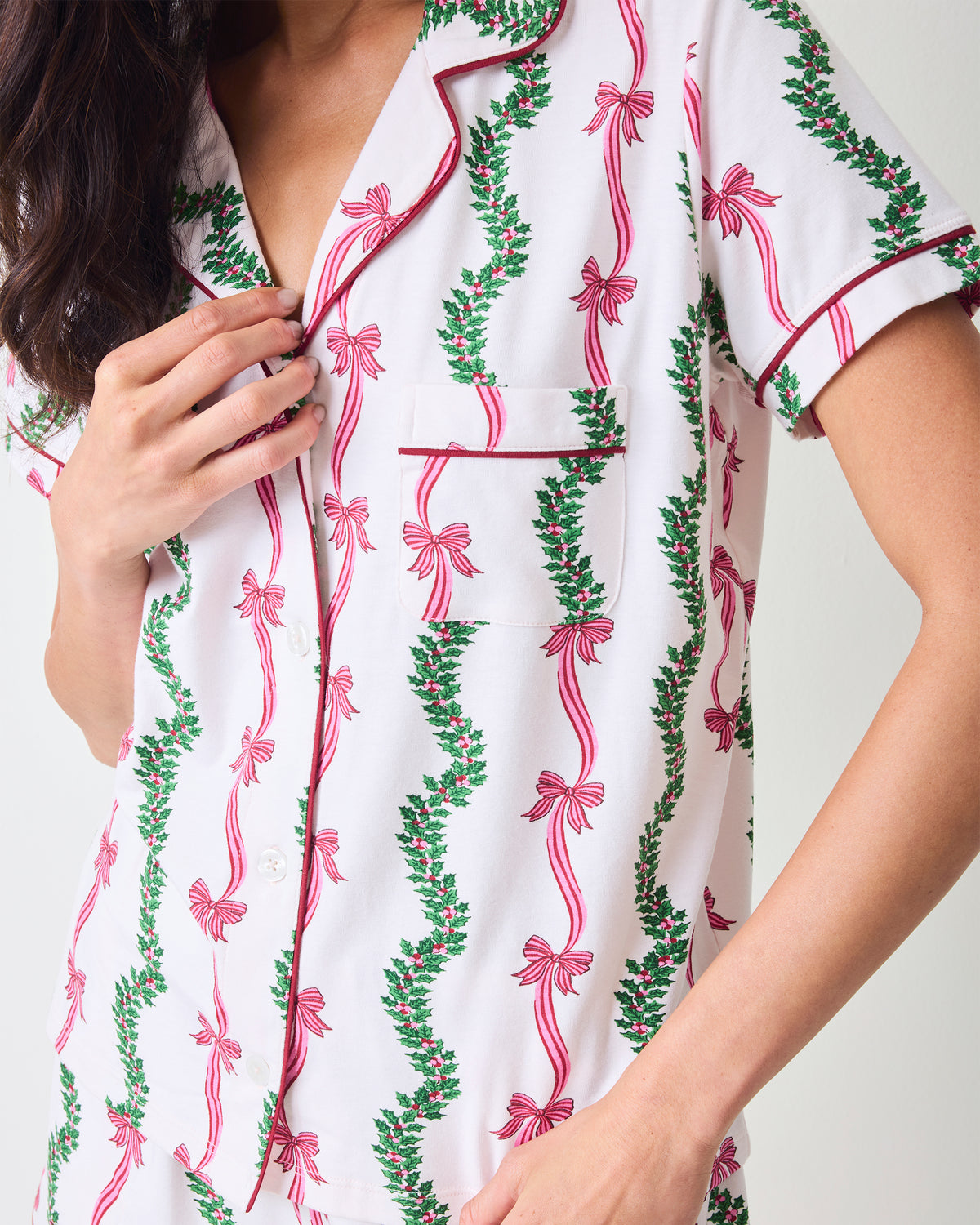 Close-up of the Ribbons & Bows short pajama top, showing its notched collar, button front, chest pocket, and pink bow and green garland print.