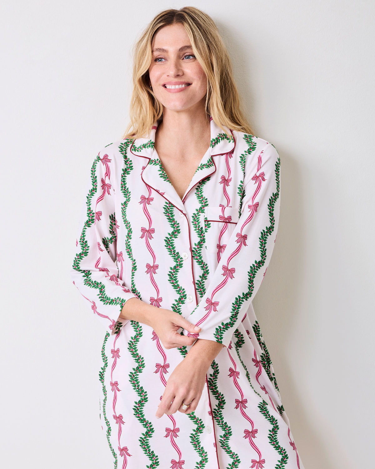 Model wearing a long-sleeved button-front sleep shirt with a pink bow and green vine print on a light background.