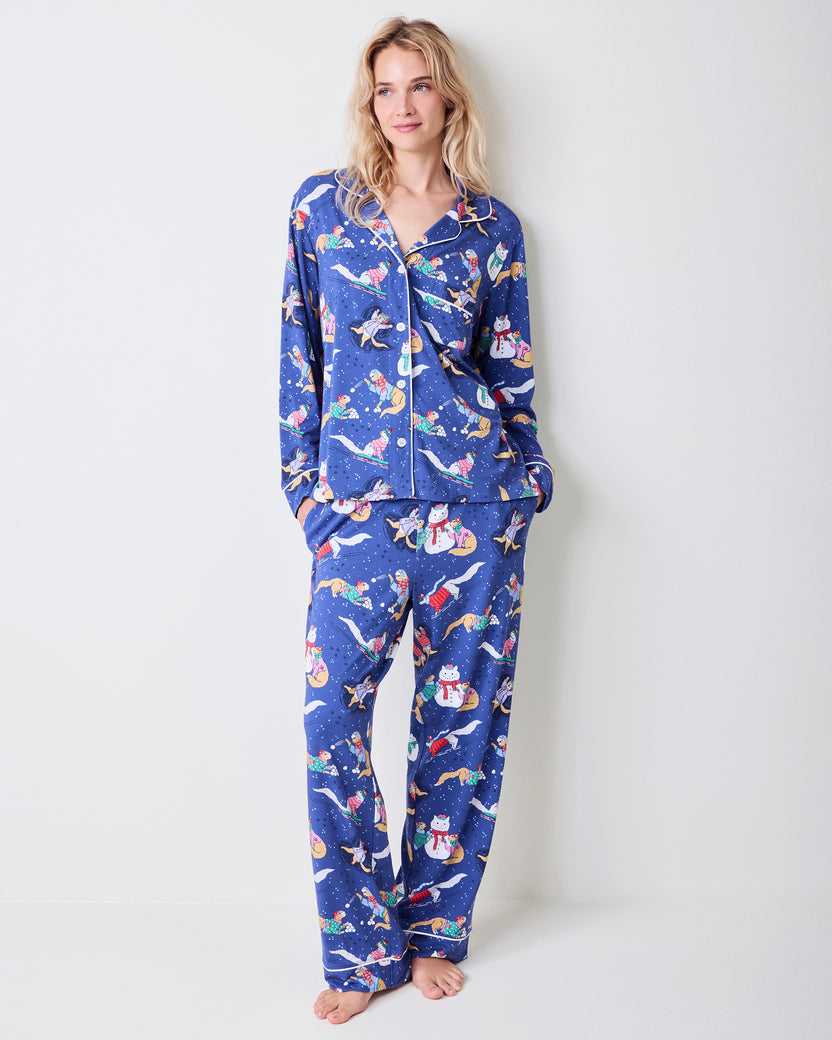 Front view of a model wearing a blue long pajama set with white piping and a cat-and-snowman winter print.