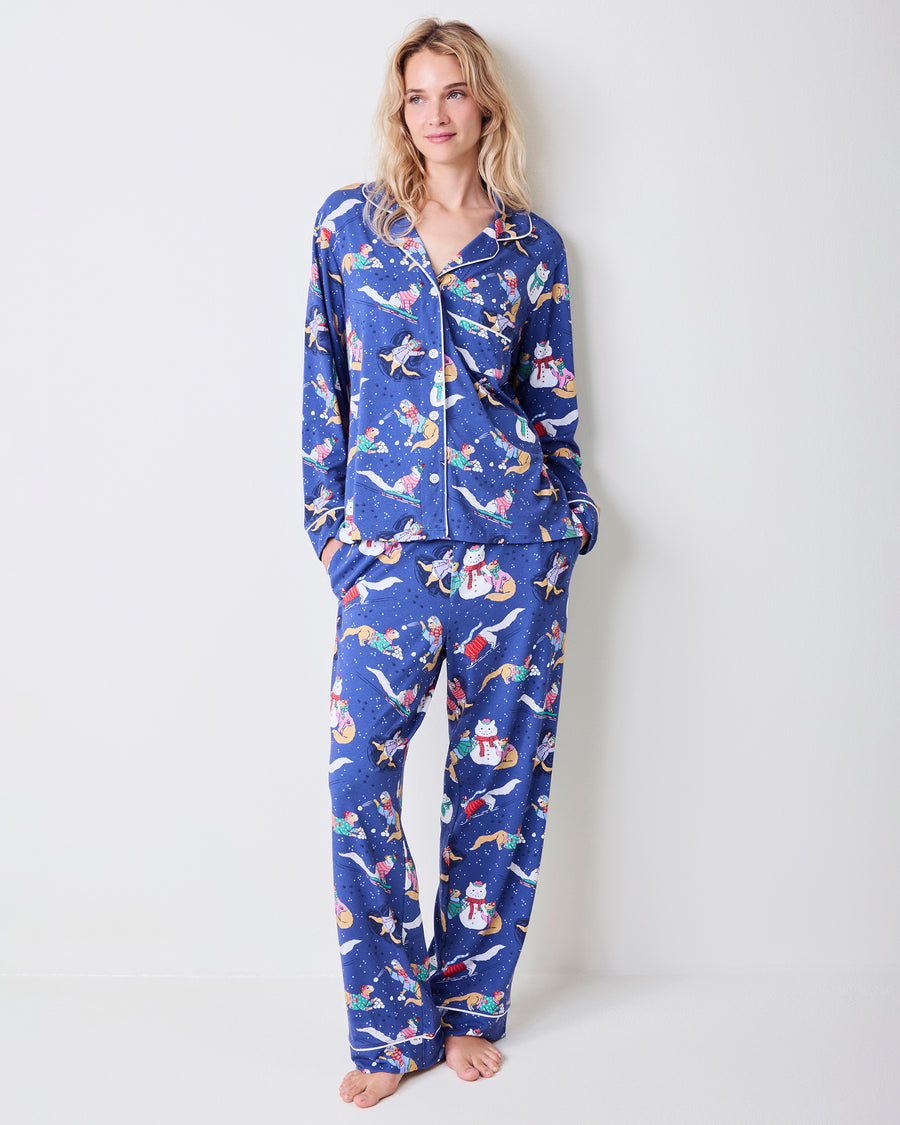 Front view of a model wearing a blue long pajama set with white piping and a cat-and-snowman winter print.