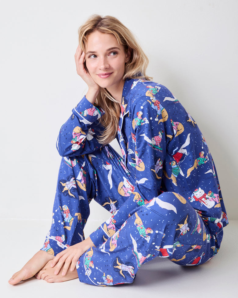 Model seated wearing the blue long pajama set with white piping and a winter print of cats and snowmen.