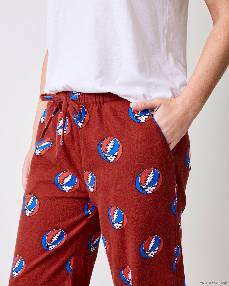 Close-up of red pajama pants showing the elastic drawstring waist, side pocket, and skull-and-lightning-bolt print.