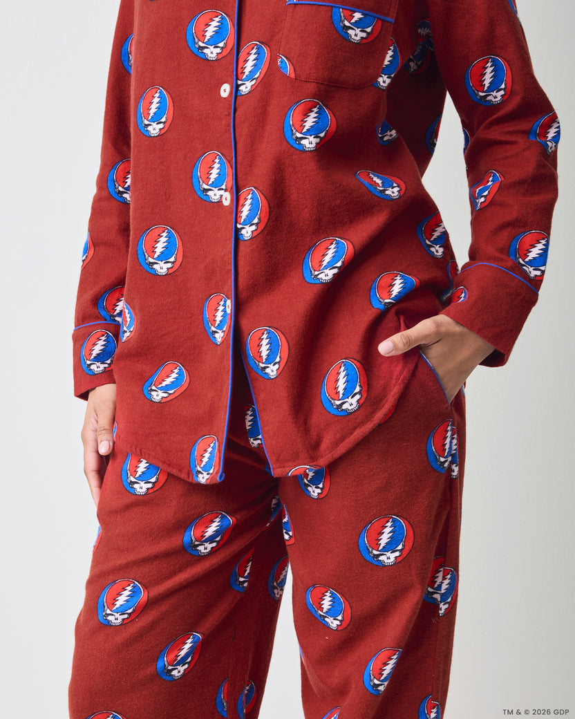 Front close-up of a red long-sleeve pajama set showing the button-front top, pockets, long pants, and skull-and-lightning-bolt print.