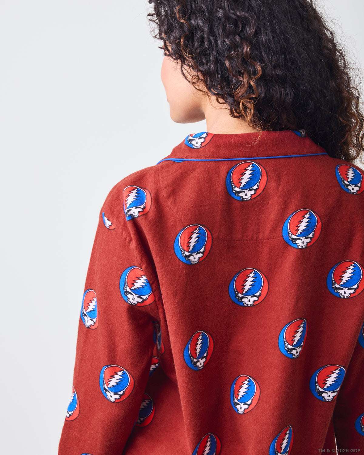 Back close-up of a red long-sleeve pajama top with blue piping and a repeated skull-and-lightning-bolt print.