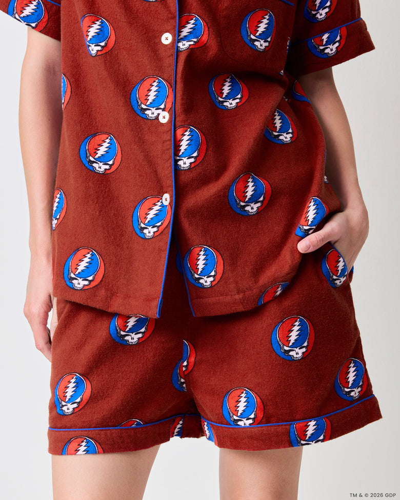 Close-up of the red short pajama set showing the skull-and-lightning-bolt print, button-front top, pocket, piping, and shorts.