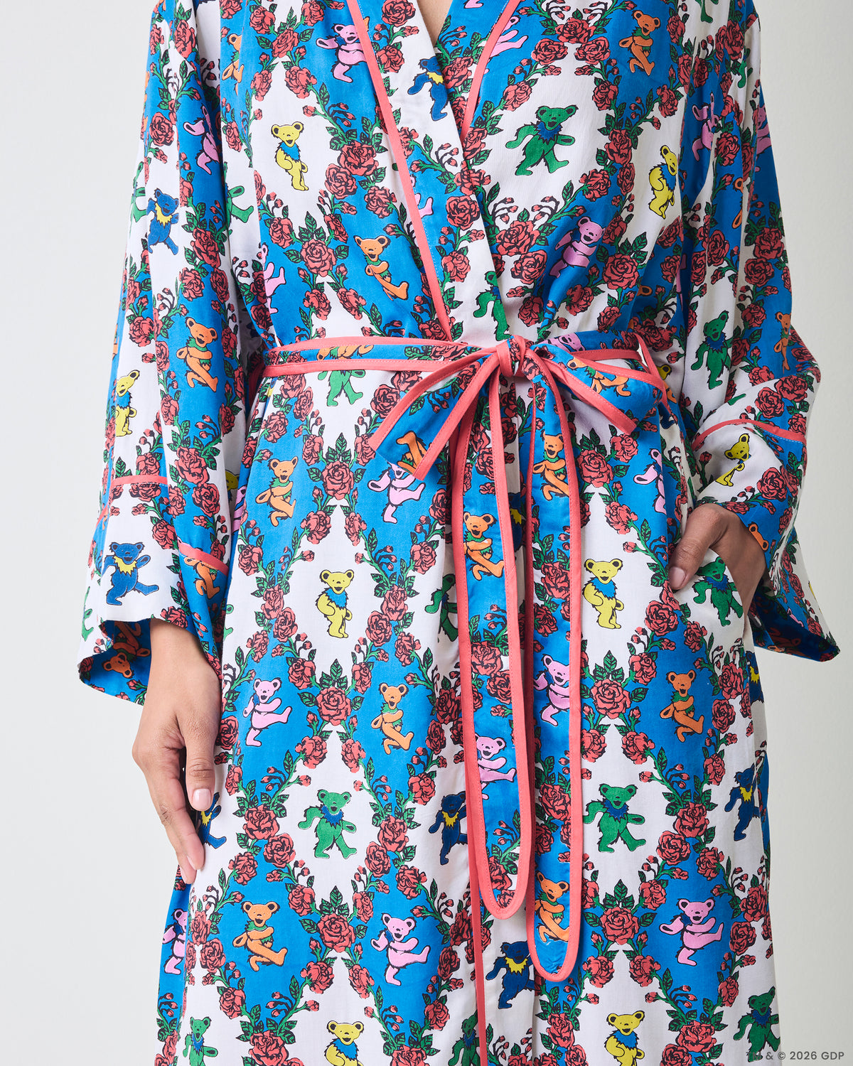 Close front detail of a robe showing the pink waist ties, trim, sleeves, and side pocket with a blue-and-white bear-and-rose print.